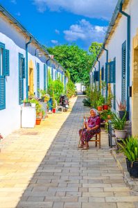 Old turkish woman is sitting on chair near houses buildings with white walls in narrow street in historical Samanbahce neighborhood